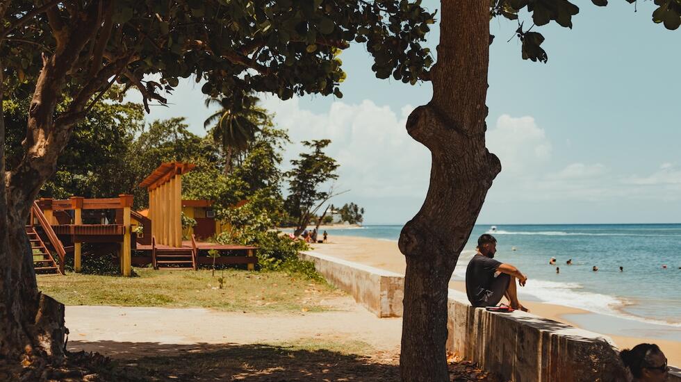 A man sits on a wall beside a Puerto Rican beach