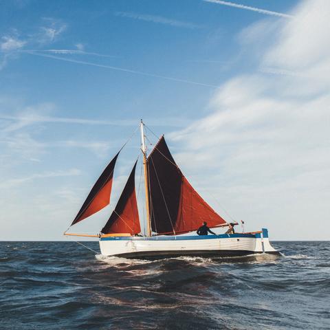 A red-sailed Norfolk Lugger sets out across the waves